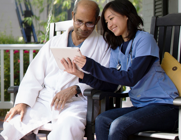 nurse and patient sitting on rocking chairs outside looking at WellSky’s home health software on a tablet