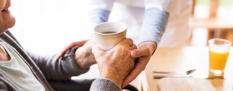 nurse helping an elderly person drink their cup of coffee