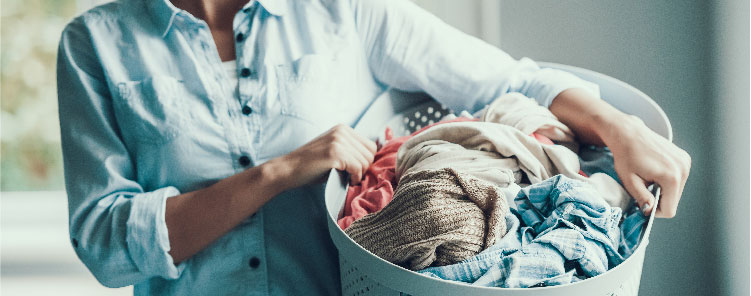 woman in denim button-up carrying a hamper of laundry